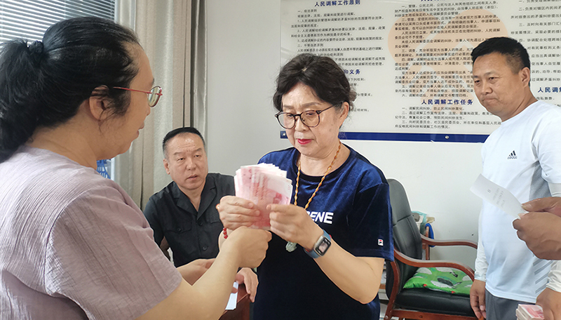 頭題片，5月30日，某藥業(yè)公司按協(xié)議約定完成第一期履行義務，將十萬現(xiàn)金交到法院，調(diào)解員付菊（左一）清點無誤之后交到農(nóng)民工委托代理人徐某手中